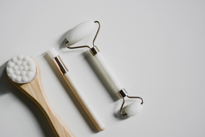 a beauty roller, makeup brush and face massager lie on a table together in a row